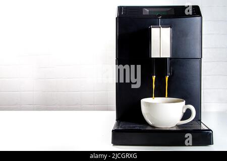 Frisch gebrühter Kaffee wird aus der Kaffeemaschine in eine weiße Keramikschale gegossen. Professionelle Kaffeemaschine für den Heimgebrauch Stockfoto