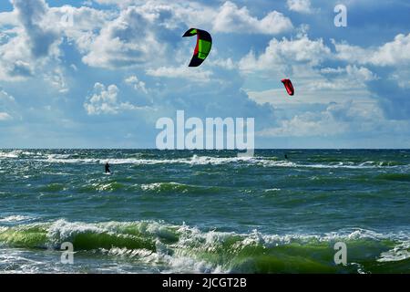 Zwei Kitesurfer gleiten bei sonnigem, windigem Wetter auf dem Meer. Wunderschöne Wolken über der Ostsee Stockfoto