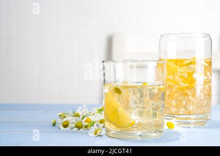 Pflanzliches organisches kaltes Getränk. Infundiert mit Blumenwasser. Iced Daisy Kamille Tee oder Limonade mit Zitronenscheibe und Eiswürfeln, in zwei verschiedenen Gläsern, blau w Stockfoto