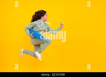 Laufen und springen. Sportbekleidung Werbekonzept. Teenager Kind Mädchen in Trainingsanzügen Jogginganzug posiert im Studio halten Fitness-Matte. Stockfoto