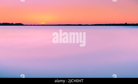 Atemberaubender Sonnenaufgang mit Pastellfarben in Blau und Orange. Langzeitbelichtung Dämmerung am See mit Blick über den niederländischen Veluwezoom am Horizont Stockfoto