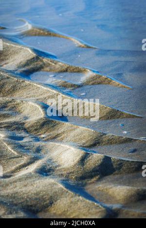 Nahaufnahme von Wasser- und Sandmustern am Sandstrand der niederländischen Nordseeküste Stockfoto