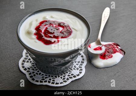 Griechischer Joghurt mit Johannisbeermarmelade in einer dunklen Schüssel auf einem schwarzen Steintisch Stockfoto