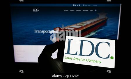 Person, die Mobiltelefon mit dem Logo von Louis Dreyfus Company BV (LDC) auf dem Bildschirm vor der Business-Webseite hält. Konzentrieren Sie sich auf die Telefonanzeige. Stockfoto