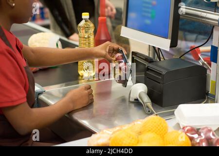 Hände einer jungen Verkäuferin, die verpackte Früchte und andere von den Käufern ausgewählte Lebensmittel im Supermarkt vor der Kasse scannt Stockfoto