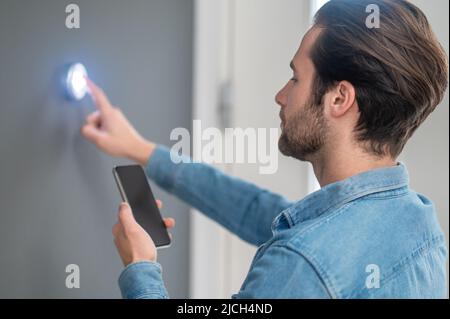 Mann mit Smartphone-Touchknopf an der Wand in Innenräumen Stockfoto