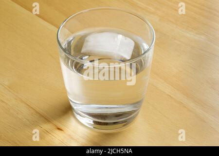 Ein einzelner Eiswürfel, der in einem Wasserglas geschmolzen und schwimmt Stockfoto