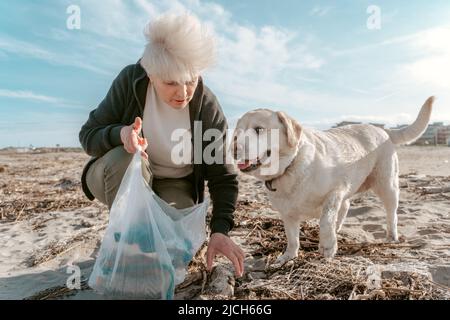 Freiwilliger und ein Hund sammeln Müll am Strand Stockfoto