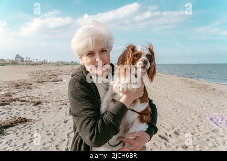 Fröhliche ältere Dame mit ihrem Haustier am Meer Stockfoto