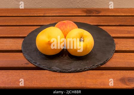 Teller mit drei reifen gelben Pfirsichen auf Holztisch Stockfoto