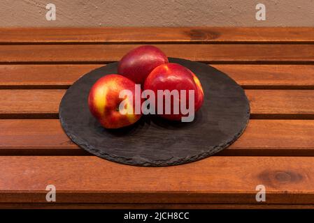 Teller mit drei Nektarinen reif und bereit, auf einem Holztisch zu essen Stockfoto