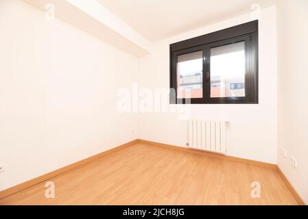 Unmöbliertes Schlafzimmer mit Buchenparkettböden, passenden Sockelleisten, dunkelbraunem Aluminiumfenster und weißem Aluminiumheizkörper darunter Stockfoto