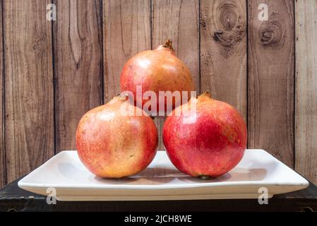 Teller mit drei reifen Granatäpfeln und dunklem Holzhintergrund Stockfoto