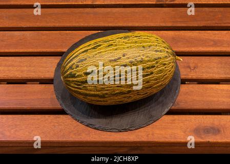 Ganze reife Melone piel de sapo auf runder schwarzer Schieferplatte Stockfoto