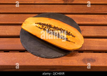Halbreife kanarische Papaya auf runder schwarzer Schieferplatte und Holztisch Stockfoto