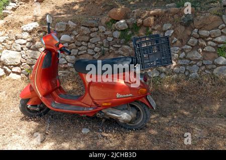 Orangefarbener Vespa-Roller, der in der Nähe einer trockenen Steinmauer an der Straße, Tilos-Insel Dodekanese, in der Nähe von Rhodos Griechenland geparkt ist Stockfoto