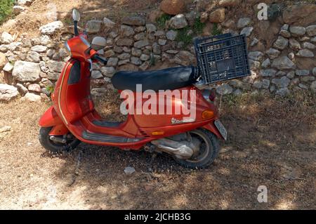 Orangefarbener Vespa-Roller, der in der Nähe einer trockenen Steinmauer an der Straße, Tilos-Insel Dodekanese, in der Nähe von Rhodos Griechenland geparkt ist Stockfoto