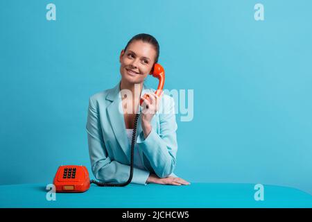 Frau, die über dem Telefon über einem blauen Hintergrund, Konzept, lächelnd Stockfoto