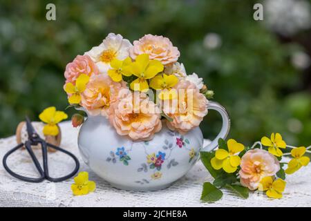 Bouquet von Aprikosenrosen und gelben Viola-Blüten in Jahrgangsmilchkanne Stockfoto