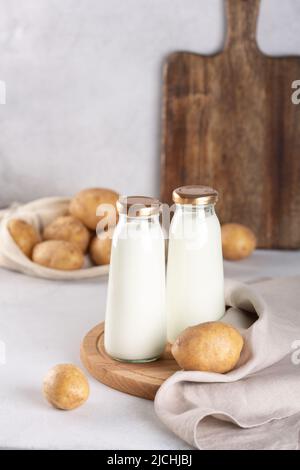 Vegane Milch auf pflanzlicher Basis in zwei Glasflaschen. Alternative Kartoffelmilch und Kartoffelknollen auf grauem Tisch Stockfoto