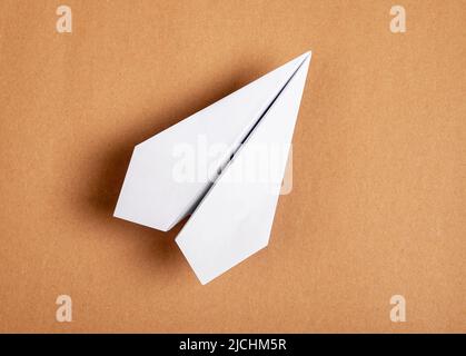 Weißes Origami-Flugzeug auf braunem Hintergrund. Papierfaltung Kunst. Architekturmodell. Hochwertige Fotos Stockfoto