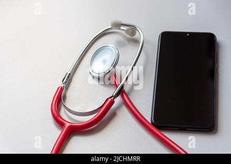 Das rote Stethoskop auf dem schwarzen Smartphone stellt Gesundheitsakten und digitale Patientenakten mit mobilen Geräten für die digitale Diagnose von Ärzten dar Stockfoto