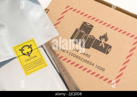 Versilberter antistatischer Kunststoffverpackungsbeutel mit einem antistatischen Warnsymbol und Kartonverpackung mit einem Warnsymbol für die Batteriegefahr nach UN 3480. Stockfoto