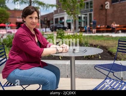 Glückliche, reife Frau, die allein an einem Tisch im Freien sitzt Stockfoto