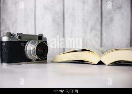 Vintage-Kamera neben einem offenen Buch auf hellem Hintergrund Stockfoto
