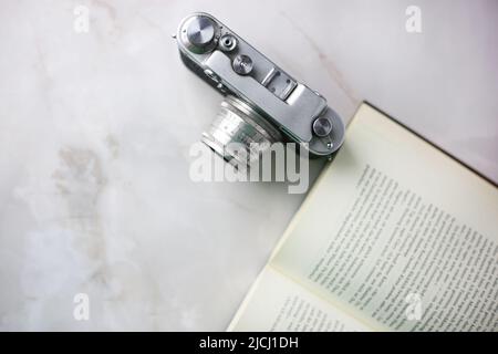 Vintage-Kamera neben einem offenen Buch auf hellem Hintergrund Stockfoto