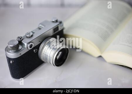 Vintage-Kamera neben einem offenen Buch auf hellem Hintergrund Stockfoto
