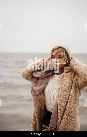 Porträt einer jungen lächelnden Frau Gesicht teilweise mit fliegenden Haaren in windigen Tag bedeckt. Ziemlich lässige Blondine auf dem Hintergrund des Meeres. Im Freien. Stockfoto