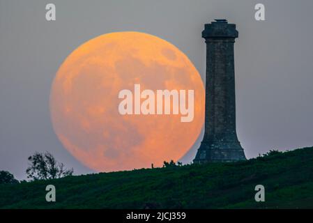 Portesham, Dorset, Großbritannien. 13.. Juni 2022. Wetter in Großbritannien. Der fast volle Strawberry Super Moon leuchtet orange, als er sich hinter dem Hardy Monument in Portesham in Dorset erhebt. Das Denkmal wurde 1844 in Erinnerung an den Vizeadmiral Sir Thomas Masterman Hardy errichtet, der Flaggenkapitän der HMS Victory bei der Schlacht von Trafalgar war. Bildnachweis: Graham Hunt/Alamy Live News Stockfoto