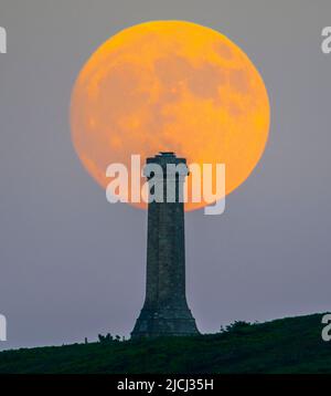 Portesham, Dorset, Großbritannien. 13.. Juni 2022. Wetter in Großbritannien. Der fast volle Strawberry Super Moon leuchtet orange, als er sich hinter dem Hardy Monument in Portesham in Dorset erhebt. Das Denkmal wurde 1844 in Erinnerung an den Vizeadmiral Sir Thomas Masterman Hardy errichtet, der Flaggenkapitän der HMS Victory bei der Schlacht von Trafalgar war. Bildnachweis: Graham Hunt/Alamy Live News Stockfoto