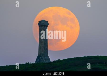 Portesham, Dorset, Großbritannien. 13.. Juni 2022. Wetter in Großbritannien. Der fast volle Strawberry Super Moon leuchtet orange, als er sich hinter dem Hardy Monument in Portesham in Dorset erhebt. Das Denkmal wurde 1844 in Erinnerung an den Vizeadmiral Sir Thomas Masterman Hardy errichtet, der Flaggenkapitän der HMS Victory bei der Schlacht von Trafalgar war. Bildnachweis: Graham Hunt/Alamy Live News Stockfoto