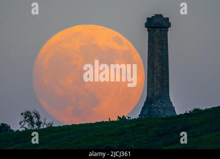 Portesham, Dorset, Großbritannien. 13.. Juni 2022. Wetter in Großbritannien. Der fast volle Strawberry Super Moon leuchtet orange, als er sich hinter dem Hardy Monument in Portesham in Dorset erhebt. Das Denkmal wurde 1844 in Erinnerung an den Vizeadmiral Sir Thomas Masterman Hardy errichtet, der Flaggenkapitän der HMS Victory bei der Schlacht von Trafalgar war. Bildnachweis: Graham Hunt/Alamy Live News Stockfoto