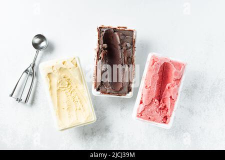 Echtes italienisches handwerkliches Eis in Verpackung: Schokolade, Erdbeeren, Vanille mit Beeren und einem Löffel Stockfoto
