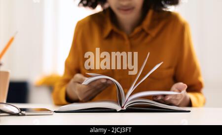 Bildung und Freizeit. Junge schwarze Frau, die Buch liest oder Notizen auf einem Notizblock schreibt, sitzt am Schreibtisch in der Bibliothek Stockfoto