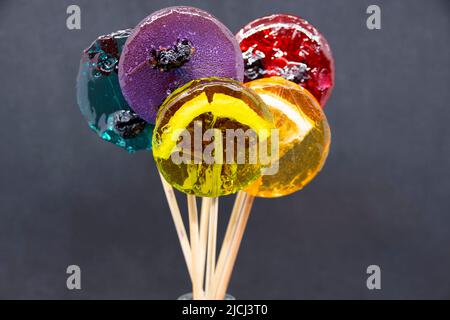 Farbige Lutscher mit verschiedenen Beeren und Früchten innen in Nahaufnahme auf grauem Hintergrund. Stockfoto