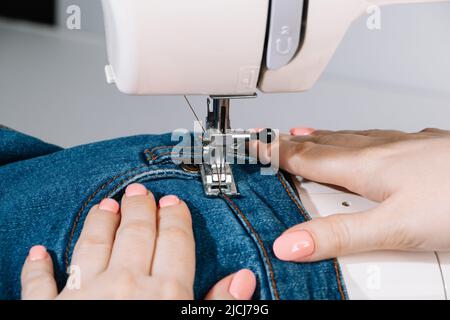 Frau Schneider arbeitet an Nähmaschine. Material mit Händen. Welt Schneider Tag. Nahaufnahme des Nähprozesses. Reparatur von Heimkleidung. Stockfoto