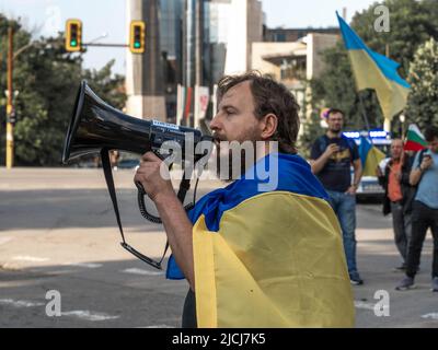 Sofia, Bulgarien, 13. Juni 2022: Ein bärtiger Mann, in ukrainische Flagge gehüllt, mit einem Lautsprecher in der Hand, spricht beim Treffen gegen den Krieg in Ukrain Stockfoto