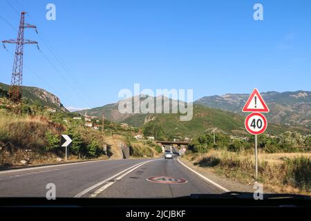 Albanien - 15.07.2017: Typische Intercity-Straße in Albanien mit Geschwindigkeitsbegrenzung 40 Zeichen, Warnschild, doppelte weiße Linien, aus dem fahrenden Auto gefangen Stockfoto