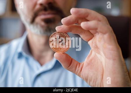 Porträt eines lächelnden Geschäftsmannes, der Bitkoin in der Büroeinrichtung hält. Bitcoins als Zahlung verwenden. Investitionen in Kryptowährungen. Kaufen und Verkaufen Stockfoto