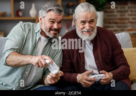 Erwachsener Sohn und älterer Vater Spaß haben, genießen Sie die Zeit zusammen zu verbringen. Zwei Generationen Familie spielen Videospiele mit Gamepads zu Hause. Vatertag Stockfoto