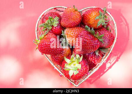 Leuchtend rote Erdbeeren in einem herzförmigen Drahtkorb auf weißem Hintergrund Stockfoto