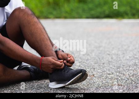 Nahaufnahme Asian Sport Läufer schwarzer Mann sitzen Schnürsenkel versuchen Laufschuhe immer bereit für Joggen und laufen auf der Straße im Freien, Gesundheit Übung w Stockfoto