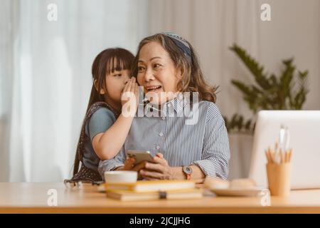 Glückliche Momente der Enkelin umarmen sich, während eine asiatische Geschäftsfrau zu Hause arbeitet. Familienkonzept. Stockfoto