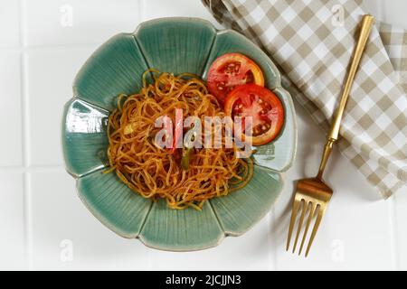 Draufsicht würziger Bihun Goreng oder gebratener Reis Vermicelli mit Gemüse. Serviert auf grünem Teller, Blick von oben auf weißem Tisch Stockfoto