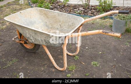 Gartenreinigungsgeräte. Ein leerer Gartenwagen in Nahaufnahme zum Transport von Gülle, Erde und Gras im Garten. Landwirtschaftliche Arbeit. Stockfoto