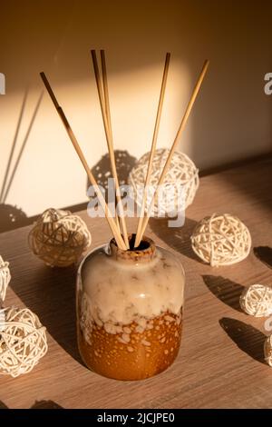 Gemütliches Zuhause Dekorationen Aroma Schilf Diffusor im Wohnzimmer. Wohnkomfort-Konzept. Flaschencontainer mit Holzstab diffundiert ätherische Öle, um Ihr minimalistisches Raumduft-Konzept zu duften. Romantisches und entspannendes Ambiente. Dekoration, Hygge und Gemütlichkeit Konzept Stockfoto
